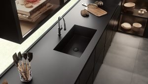 Solid Colour black kitchen worktops with kitchenware laid on top and a matching single-bowl sink and lever tap in the middle, photographed at an angle and from above. Choice of worktop for a modern kitchen.