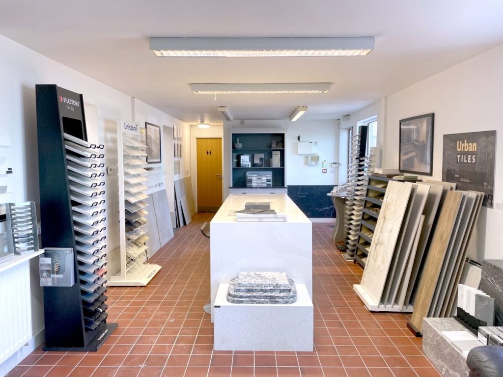 The MGD Showroom in Hereford featuring a quarry-tiled traditional floor with stone sample racks on either wall with a marble kitchen island in the middle and a seating area in the background.