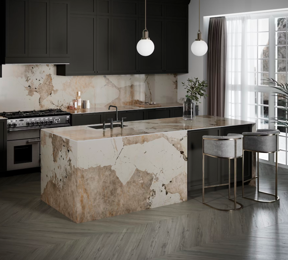 Dekton Khalo roomshot featuring oblique angled kitchen island in cream and brown stone-effect with breakfast bar end and half clad in same material. Kitchen worktop and splashback in background with dark cabinets for a modern look.