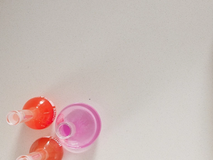 a white laboratory surface with 3 glass bottles containing purple, red and pink liquids.