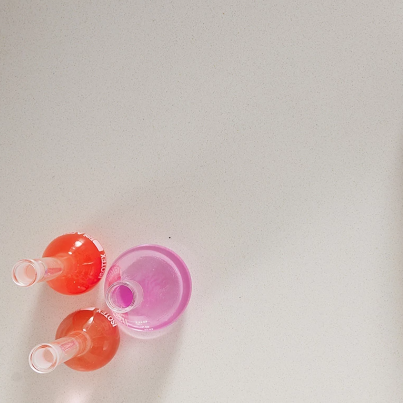 a white laboratory surface with 3 glass bottles containing purple, red and pink liquids.