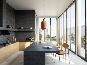 Silestone Earthis Raw D roomshot featuring a side-on kitchen breakfast bar in an open plan living space with floor-to-ceiling windows on the right and kitchen cabinets/shelves on the right, in charcoal and wood tones.